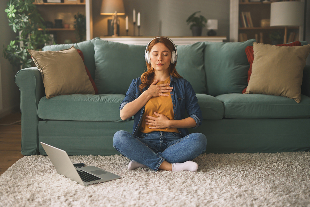 Woman meditating with headphones near laptop.