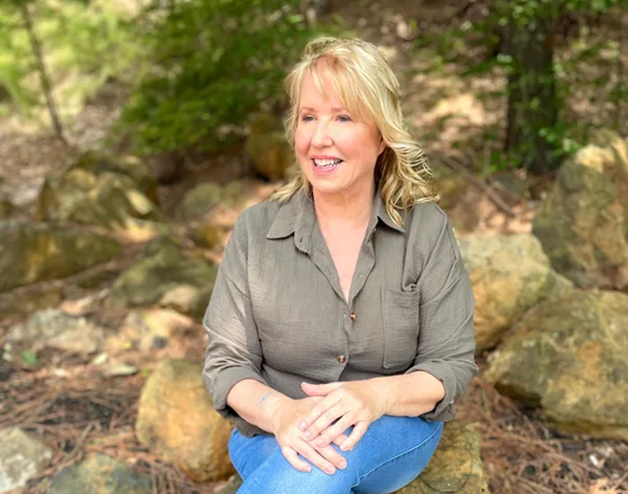 Smiling woman sitting on rocks outdoors.